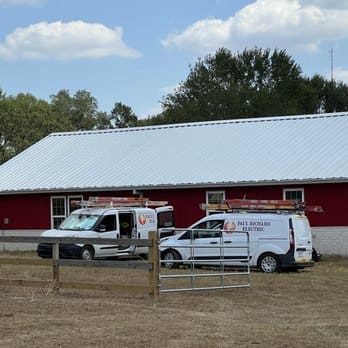 A barn with two trucks parked in front of it.