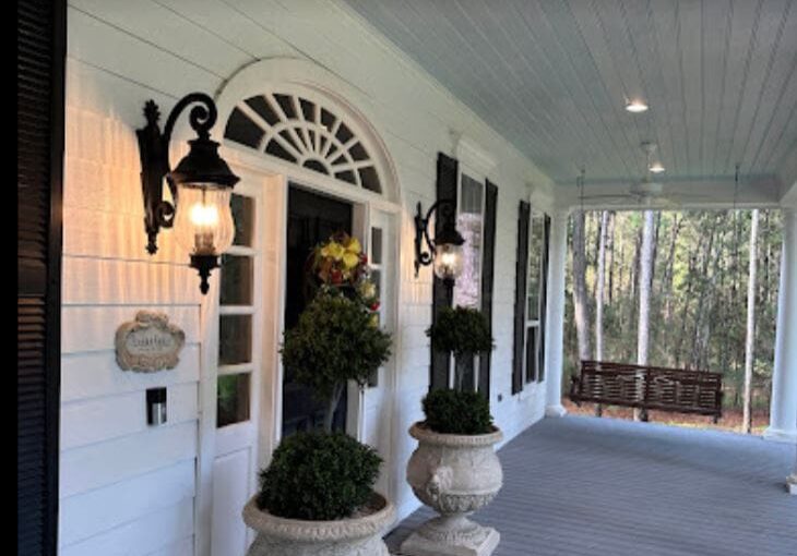 A porch with two large white urns and a swing.